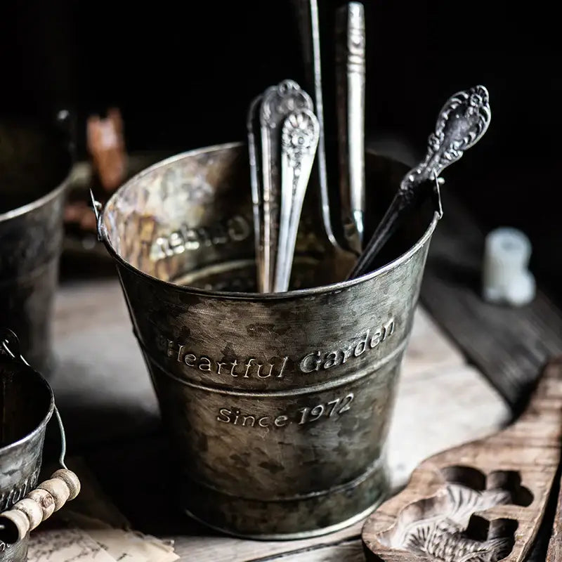 Decorbites™ vintage iron handle bucket in metallic finish engraved with heartful garden since 1972 holding ornate silver spoons