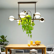 Modern black metal island lighting fixture with spherical white glass shades and hanging green plant centerpiece
