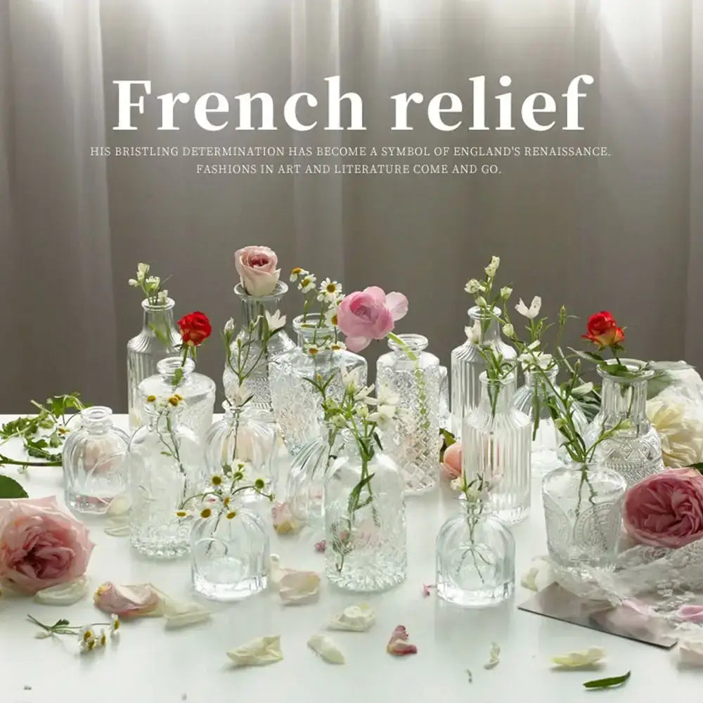 A collection of clear glass decorbites™ vintage relief vases with intricate patterns holding pink and white flowers