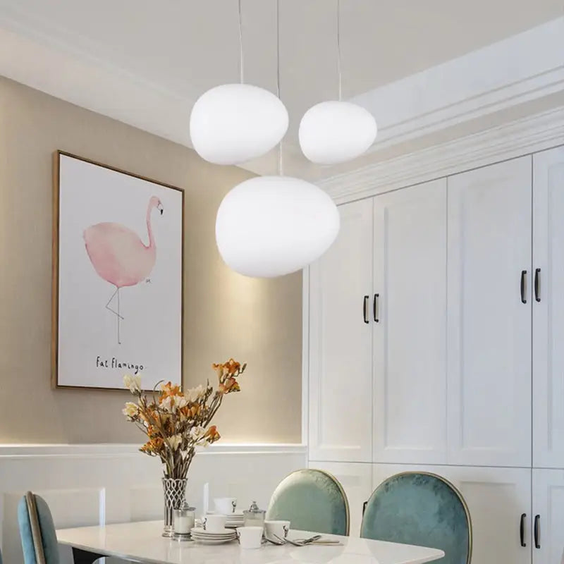 Three white glass oval pendant lights hanging from the ceiling in a simple glass oval ceiling design