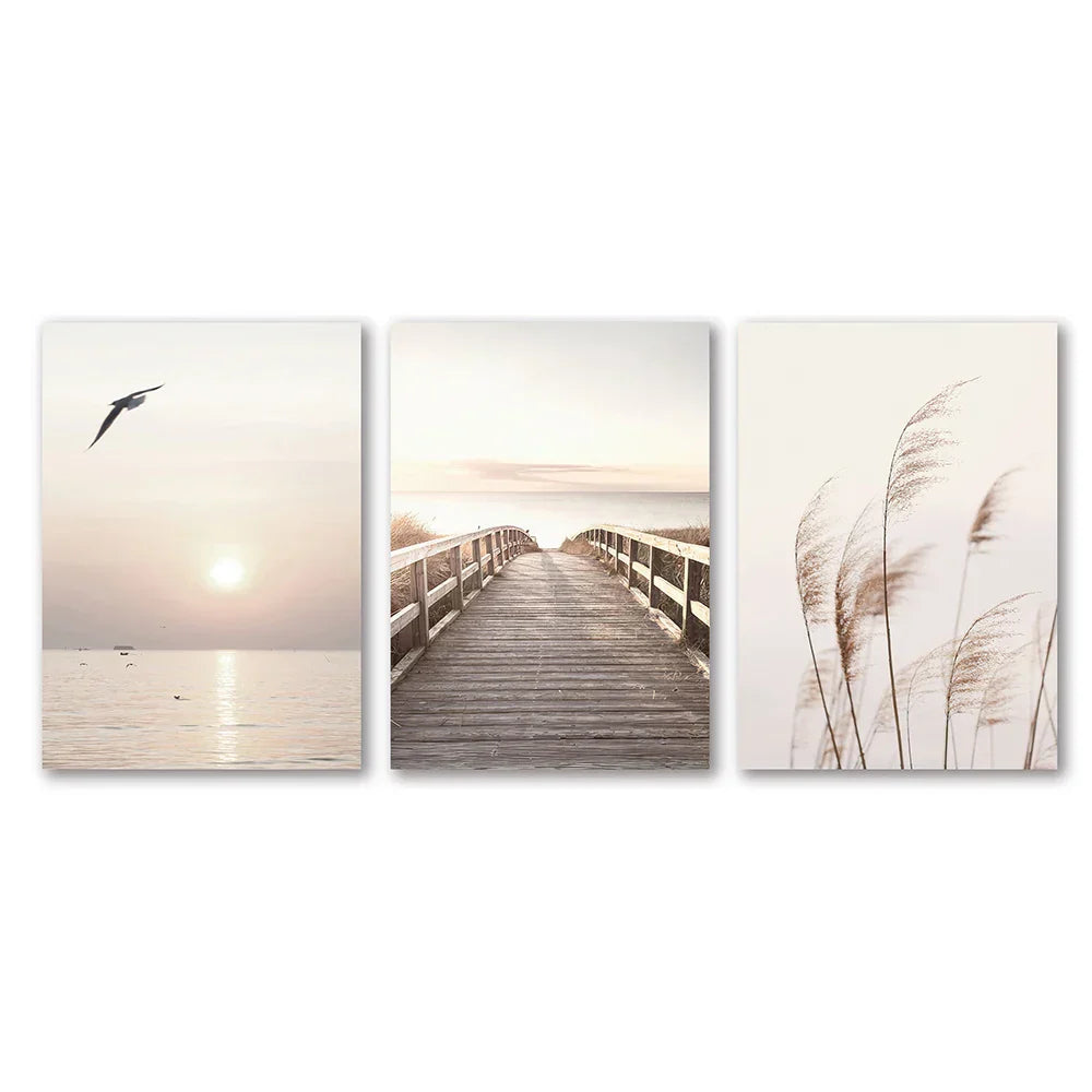 Set of three minimalist white seascape canvas prints featuring a seagull, boardwalk, and tall reeds by DecorBites™