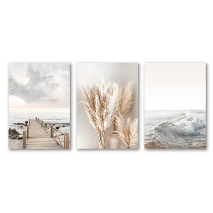 Set of three minimalist white seascape canvas prints featuring a wooden pier pampas grass and ocean waves by decorbites