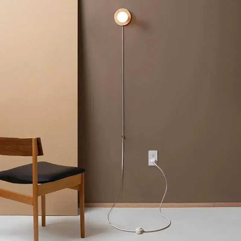 DecorBites™ wood plug-in wall sconce with circular wooden head and slender metallic stem plugged into outlet
