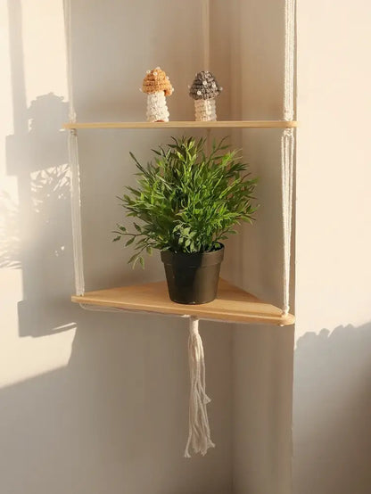 Decorbites™ wooden corner shelf with light wood slats and white macrame holding a potted plant in a black pot
