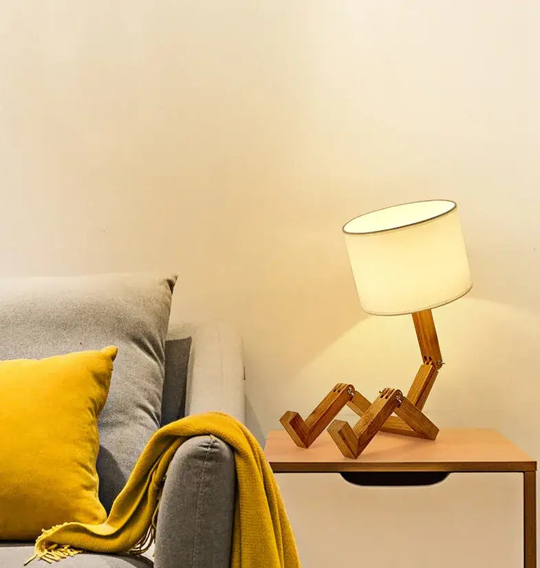 A warm-toned wooden robot shape creative table lamp with cylindrical shade on articulated wooden base for indoor use