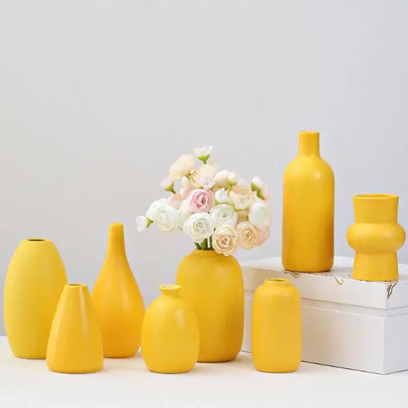 A collection of matte yellow porcelain flower vases for home decor with one holding white and pink flowers