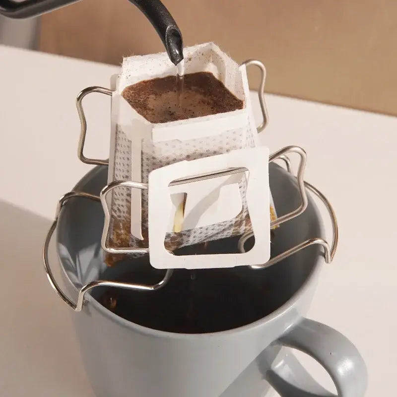 Disposable coffee filter cup with metal frame in white paper being poured into a gray ceramic mug for drip brewing