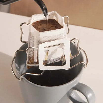 Disposable coffee filter cup with metal frame in white paper being poured into a gray ceramic mug for drip brewing