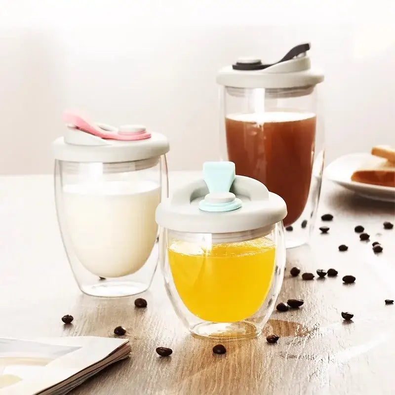 Double deck insulated clear glass tumblers with white lids and colorful spout handles filled with milk juice and coffee
