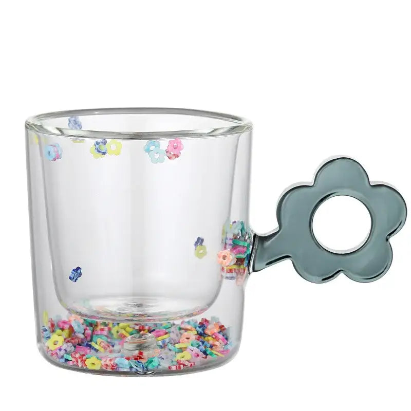 Clear double wall glass mug with a matte gray flower-shaped handle and colorful glitter flowers inside for kitchen use