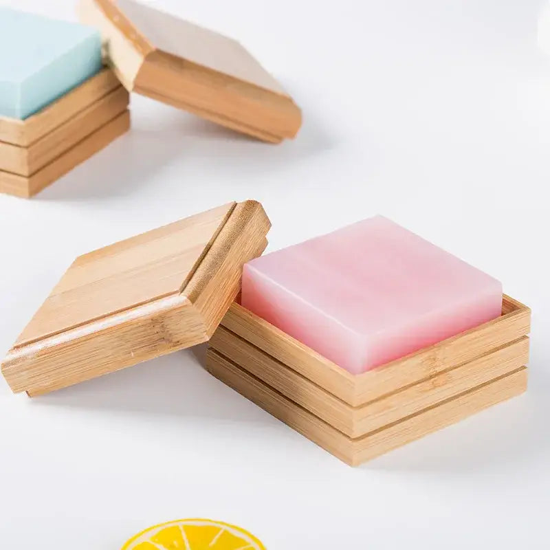Pink translucent soap bar nestled in a light wood bamboo soap dish with hinged lid for bathroom storage