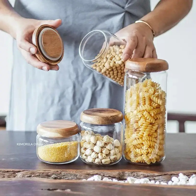 Clear glass storage jars with elegant acacia wood lids holding dry goods like pasta and grains for kitchen use