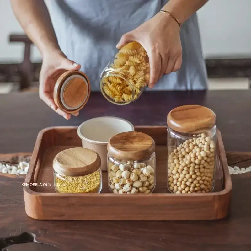 Clear glass food storage jar filled with spiral pasta featuring an elegant acacia wood lid in natural wood color