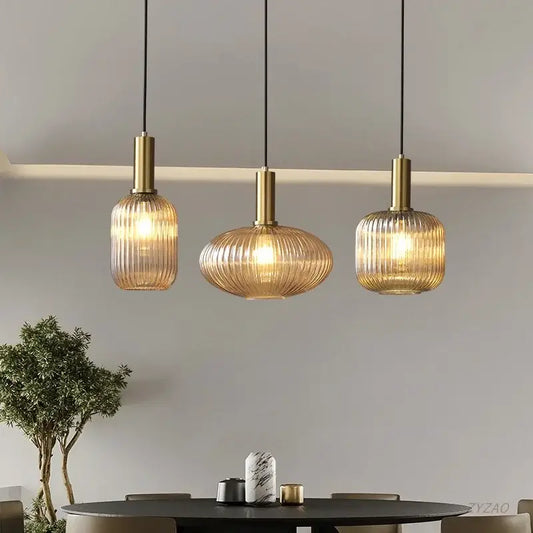 Three elegant gold-toned glass pendant lights with ribbed amber shades hang from black cords above dining table