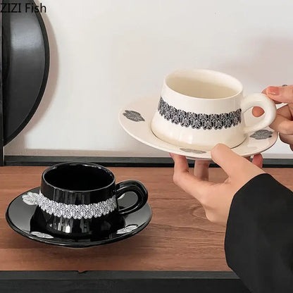 White porcelain cup and saucer set with black floral lace pattern held in hands in minimalist dining room setting