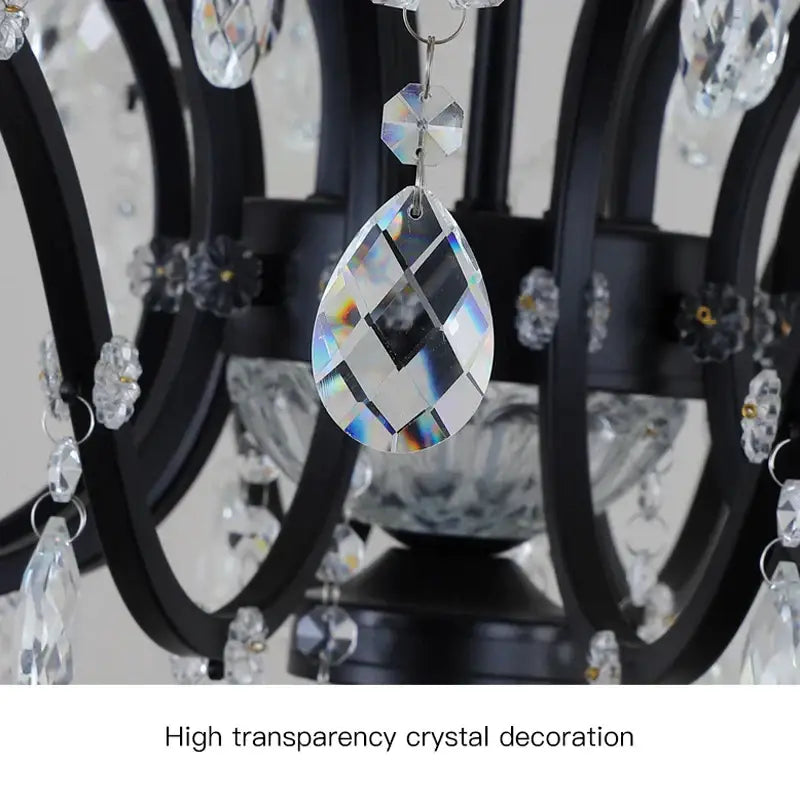 A teardrop-shaped transparent crystal pendant with faceted surfaces on a black metal crystal candle chandelier