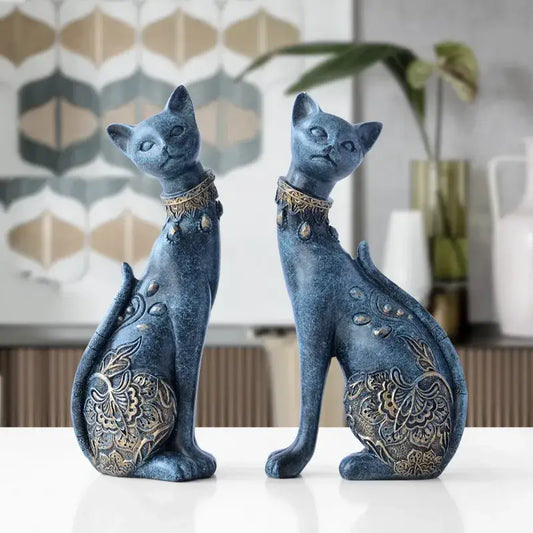 Two elegant blue and gold decorbites cat statues with intricate patterns sitting side by side on a white surface