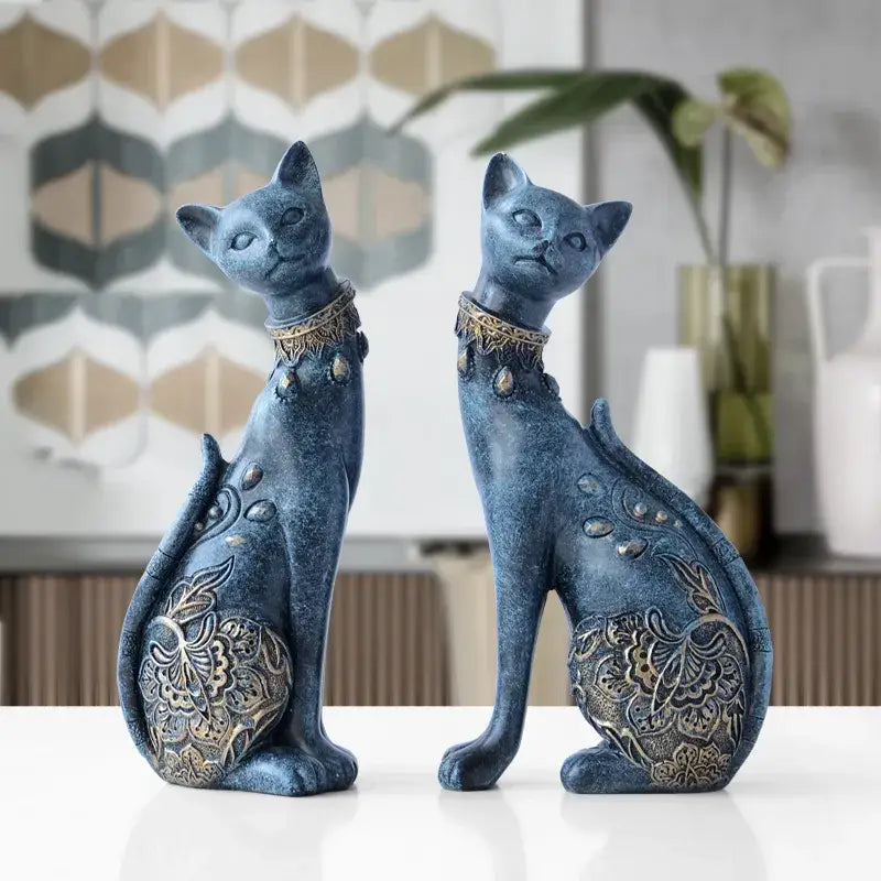 Two elegant blue and gold decorbites cat statues with intricate patterns sitting side by side on a white surface