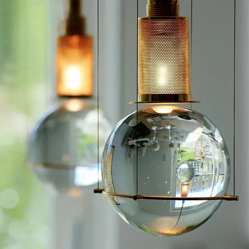 A sleek transparent glass globe pendant light with brass mesh top and support bar in elegant decorbites crystal ball led design