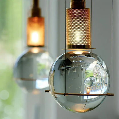 A sleek transparent glass globe pendant light with brass mesh top and support bar in elegant decorbites crystal ball led design