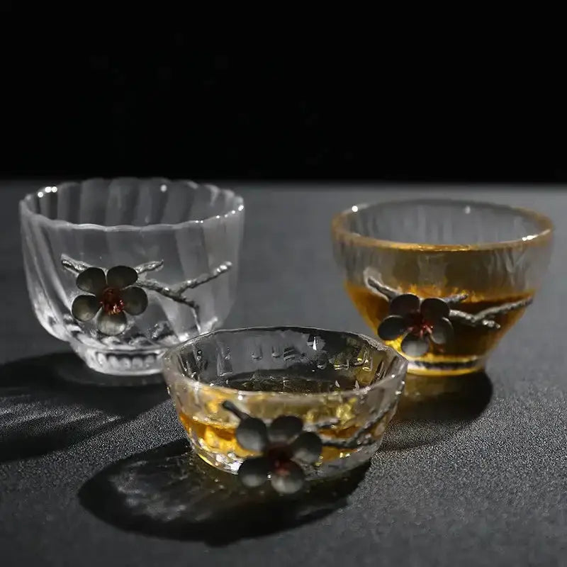 Elegant carved tin glass tea cup set with dark floral embellishments and textured rims holding amber tea