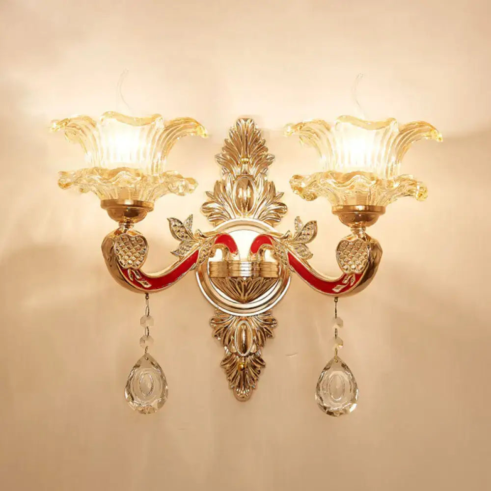 Elegant gold scrolled arm wall mount sconce with two amber glass flower shades and dangling crystal pendants for bedroom lighting