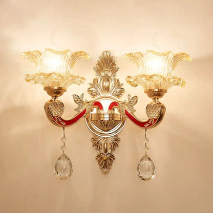 Elegant gold scrolled arm wall mount sconce with two amber glass flower shades and dangling crystal pendants for bedroom lighting
