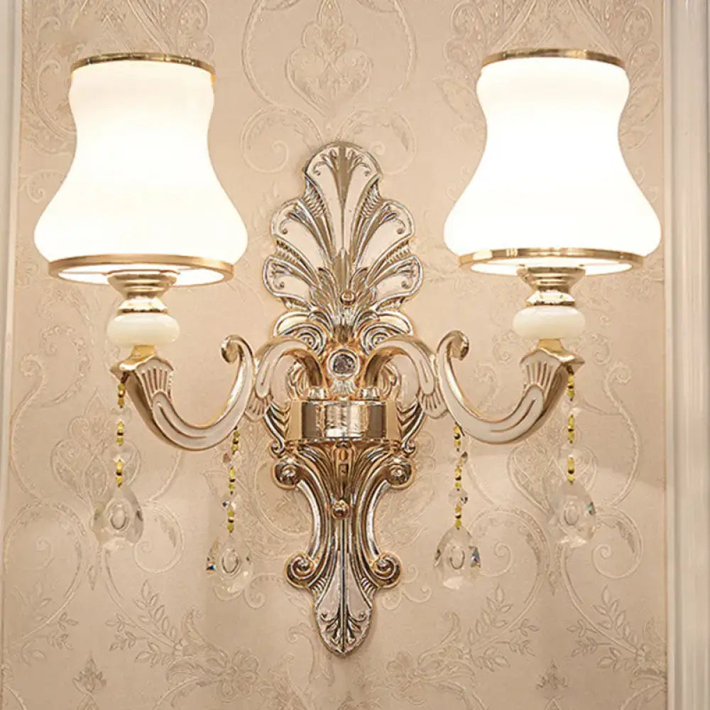 Elegant gold scrolled arm wall mount sconce with two white lampshades and crystal droplets for bedroom lighting