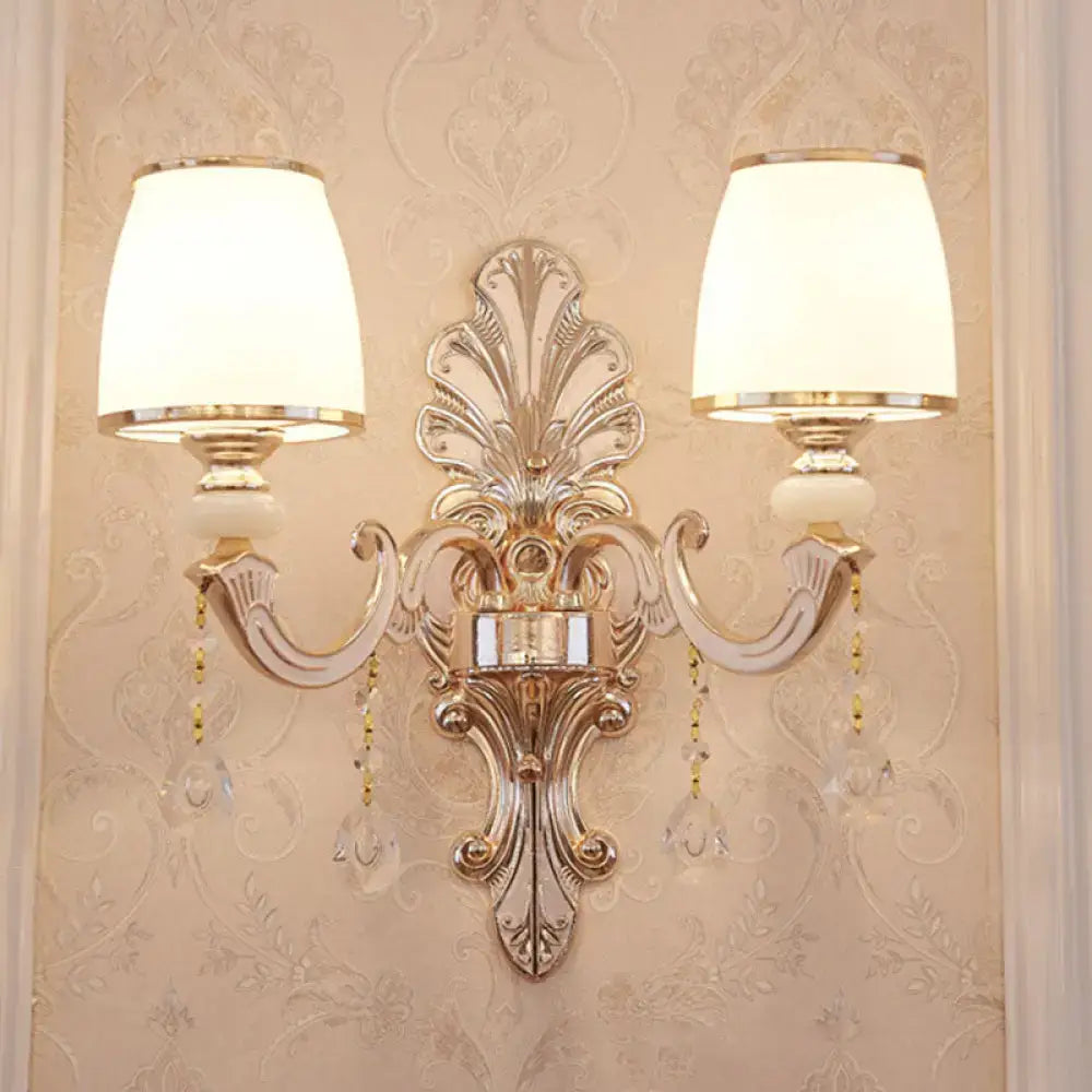 Elegant gold scrolled arm wall mount sconce with cream fabric shades and dangling crystal accents for bedroom lighting