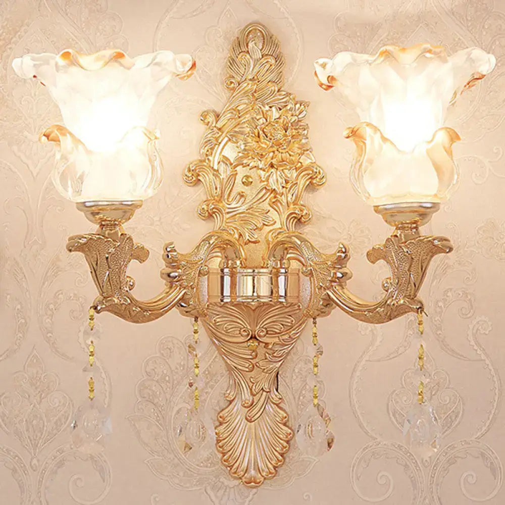 Elegant gold scrolled arm wall mount sconce with two fluted glass shades and dangling crystal beads for bedroom lighting