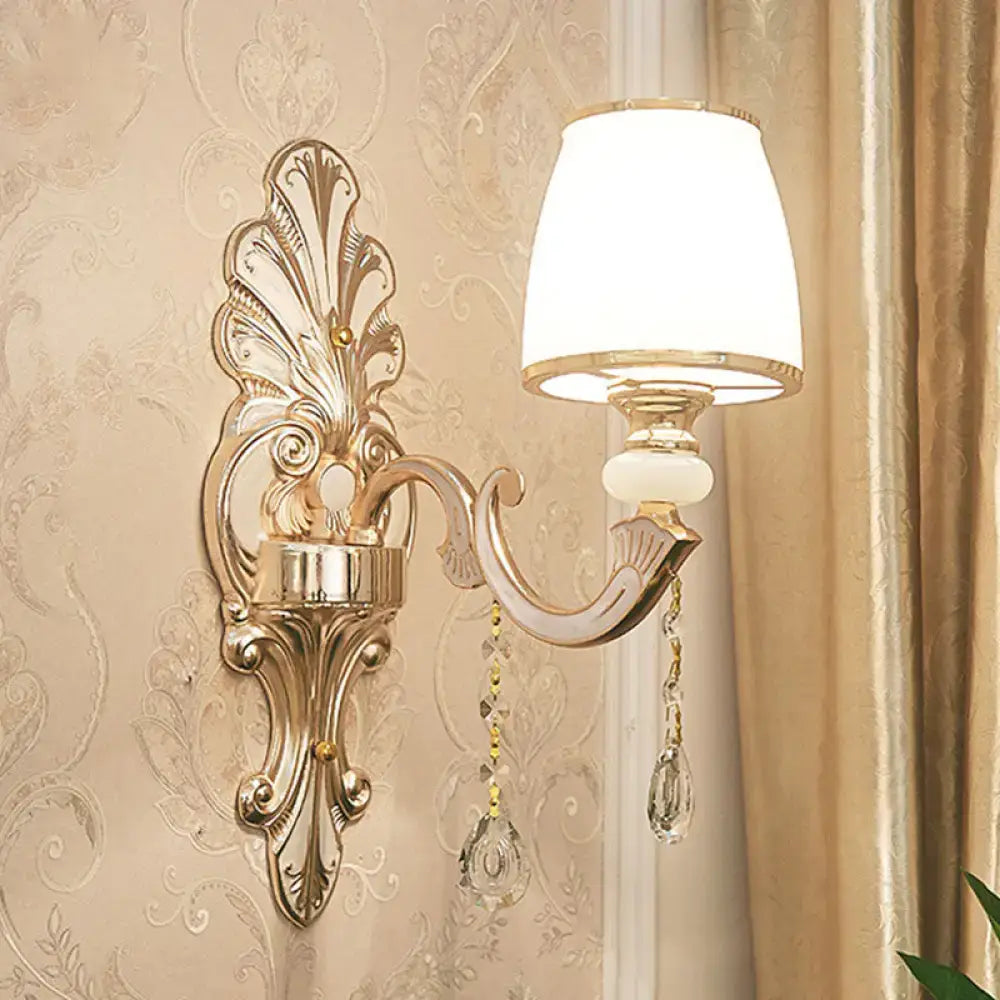 Elegant gold scrolled arm wall mount sconce with white lampshade and crystal droplets for bedroom lighting