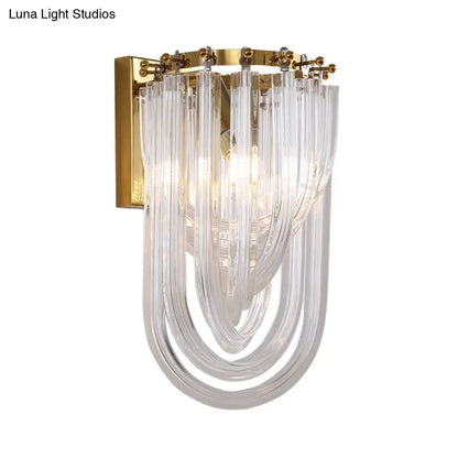 Elegant gold wall lamp with twisted crystal shade featuring clear curved glass tubes and polished brass bracket for bedroom
