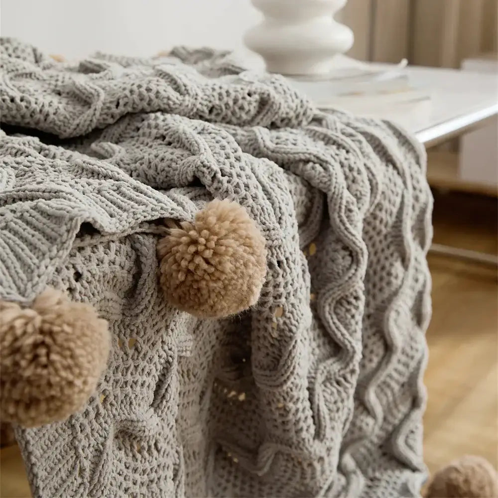 Cozy gray knitted throw blanket with cable knit pattern and elegant chenille pompons for light gray decorbites decor