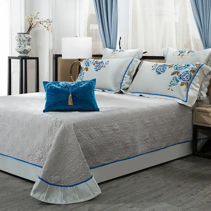 Light gray quilted bedspread with blue piping and ruffled edges in an elegant ivory and royal blue 200s embroidery egyptian cotton bedding set