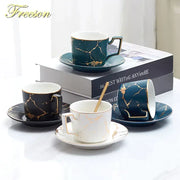 Set of four elegant ceramic tea set cups and saucers in black, deep teal, and white with gold marble pattern