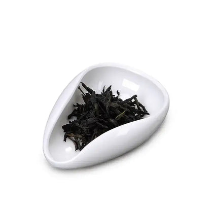 White ceramic tea scoop filled with dark curled leaves from decorbites ceramic white dose trays and tea spoon set