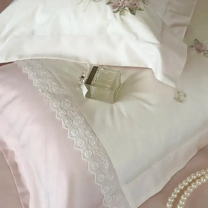 A clear glass perfume bottle with silver cap resting on white satin bedding set with decorbites flowers embroidery lace