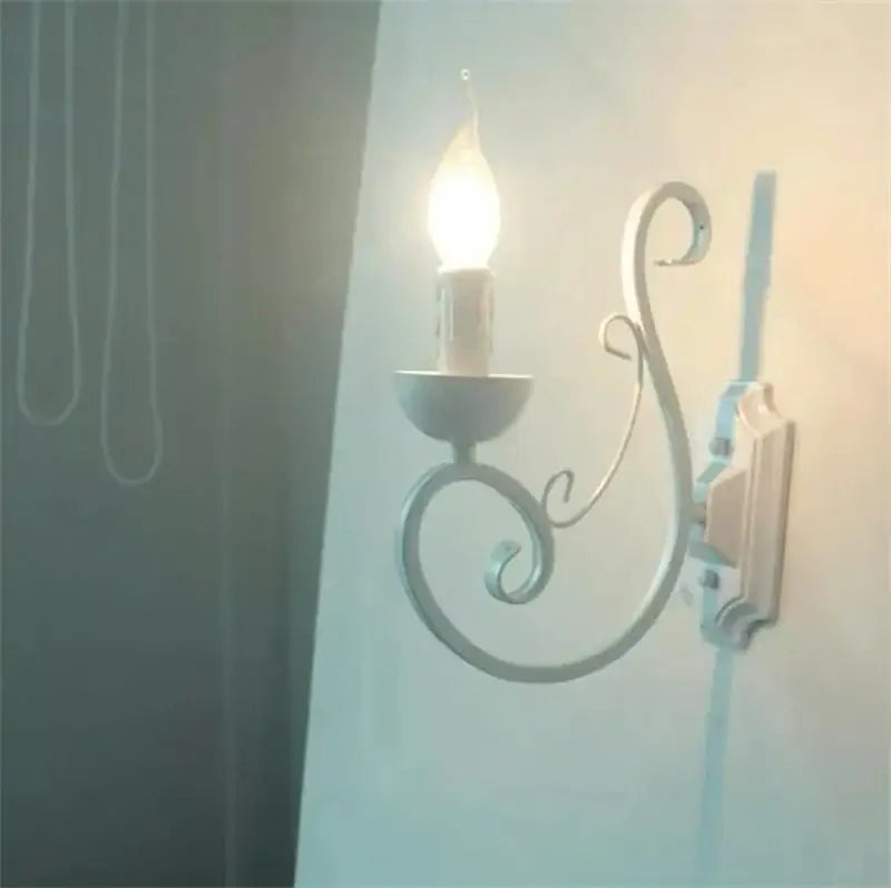 Elegant white iron wall lamp with ornate scrollwork and a lit candle-style bulb for decorbites elegant white decor