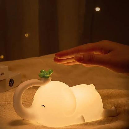 A soft glowing white decorbites elephant silicone night light with a green four-leaf clover on its trunk for bedroom decor