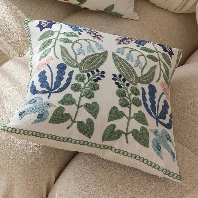 A rectangular cream office cushion pillowcase with intricate blue green and pink embroidered floral and bird patterns