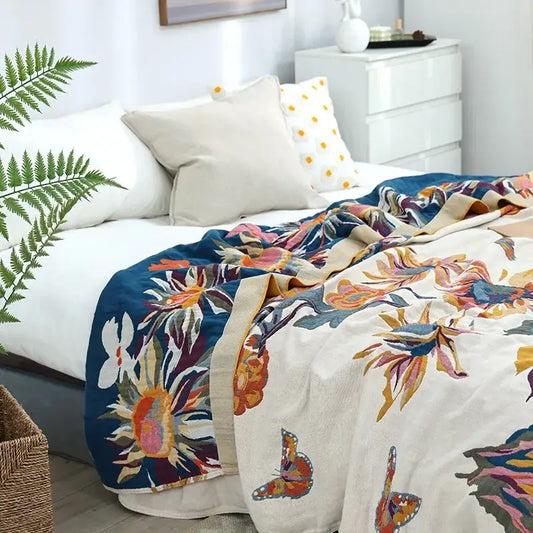 A vibrant embroidered floral and butterfly decorbites cotton gauze bedroom throw blanket in cream and bold blue accents