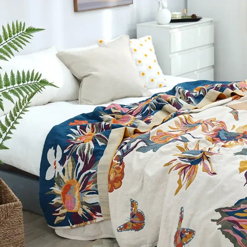 A vibrant embroidered floral and butterfly decorbites cotton gauze bedroom throw blanket in cream and bold blue accents