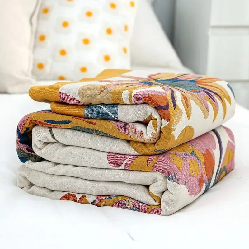 Stack of folded decorbites cotton gauze bedroom blankets with embroidered floral patterns in mustard yellow pink and blue