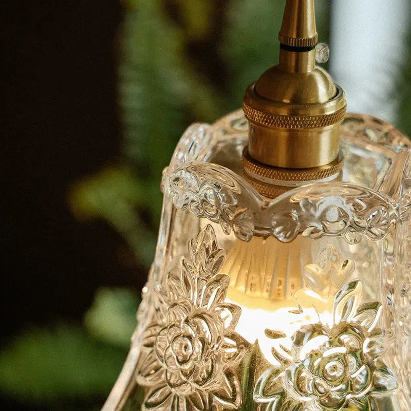 A clear glass pendant light with intricate floral etchings and polished copper metal fixture for dining room