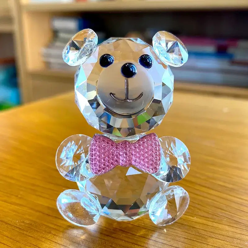 A faceted clear crystal teddy bear figurine with black button eyes and a pink bow tie for bedroom decor