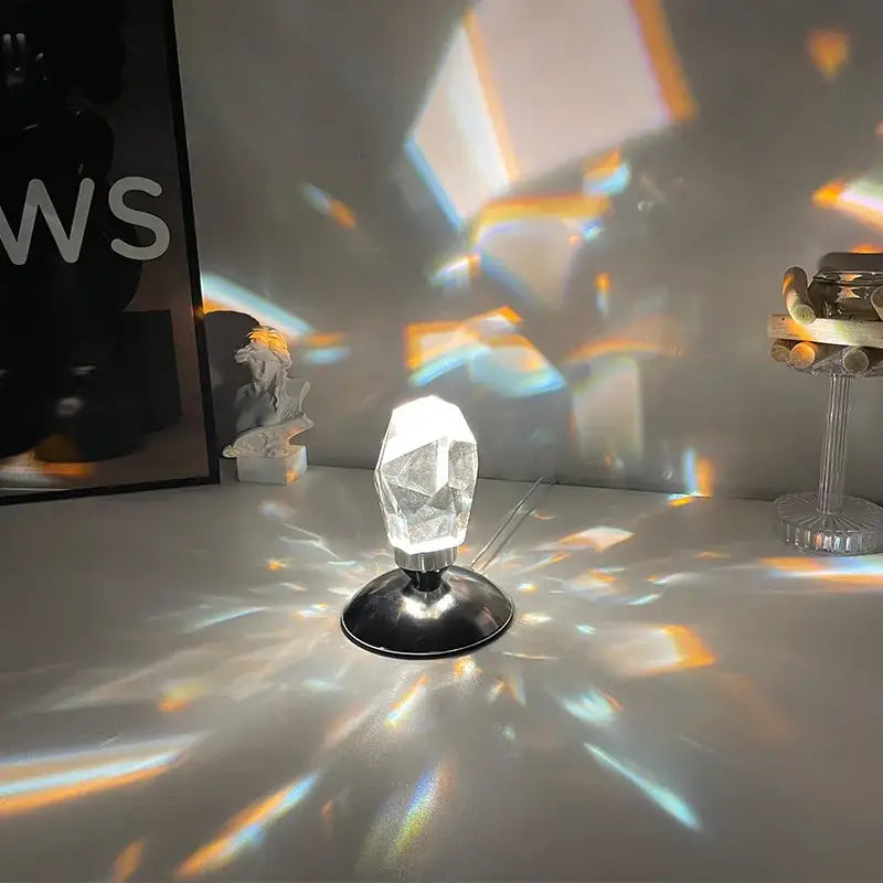 Faceted crystal diamond table lamp with clear prism and black metallic base casting colorful rainbow light patterns