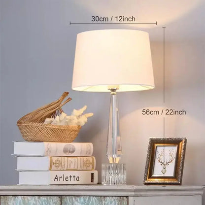 Faceted decorbites crystal table lamp with remote control featuring a clear crystal base and off-white fabric shade