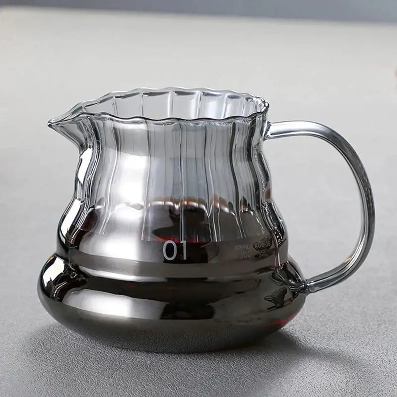 Clear glass coffee carafe with faceted diamond design, fluted rim, ribbed body, metallic base, and filter cup