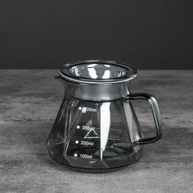 A sleek dark tinted diamond glass coffee carafe with geometric filter cup and milliliter measurement markings