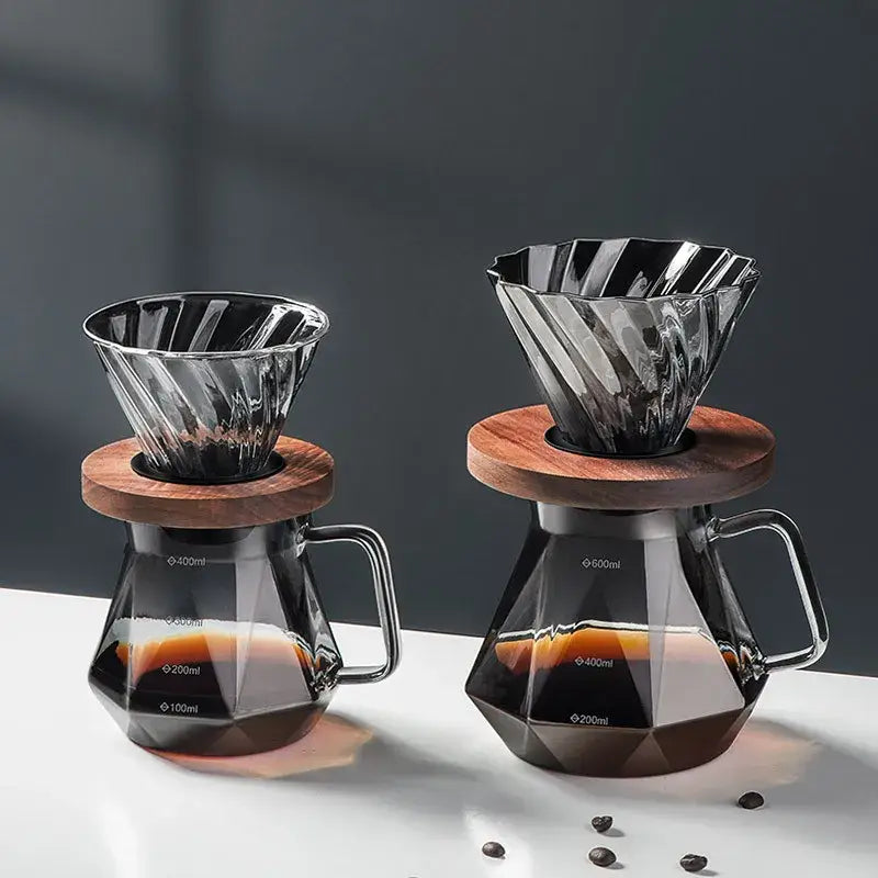 Two elegant faceted dark tinted diamond glass coffee filter cup drippers with wooden lids atop matching glass coffee carafes